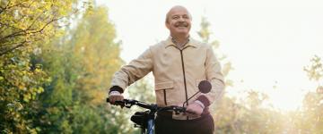 Adulto mayor en un parque sosteniendo el manubrio de su bicicleta.